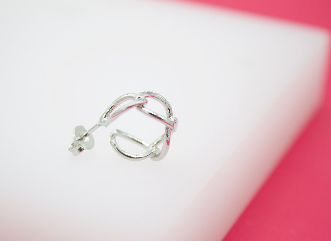 A silver hoop earring rests on a white display surface against a bright pink background.