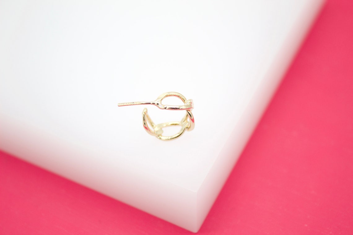 A delicate gold hoop earring rests on a white display surface against a vibrant pink background.