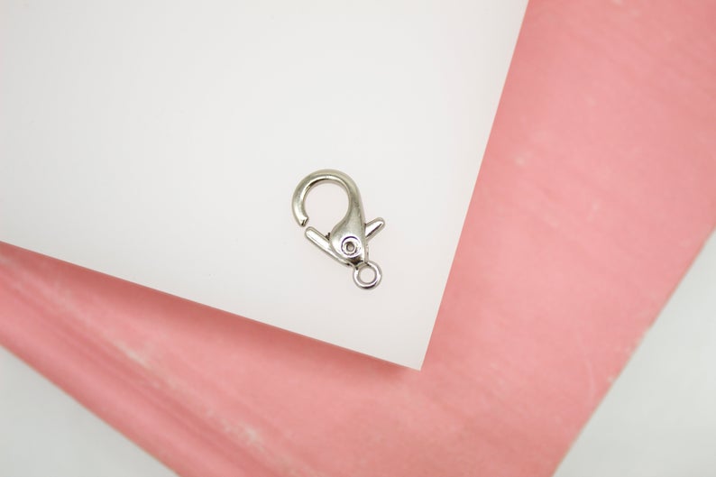 A silver lobster clasp rests on a white and pink surface.