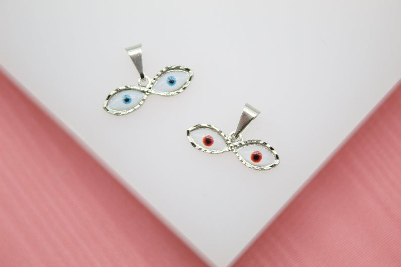 Two silver evil eye charms with blue and red enamel details rest on a white display surface.