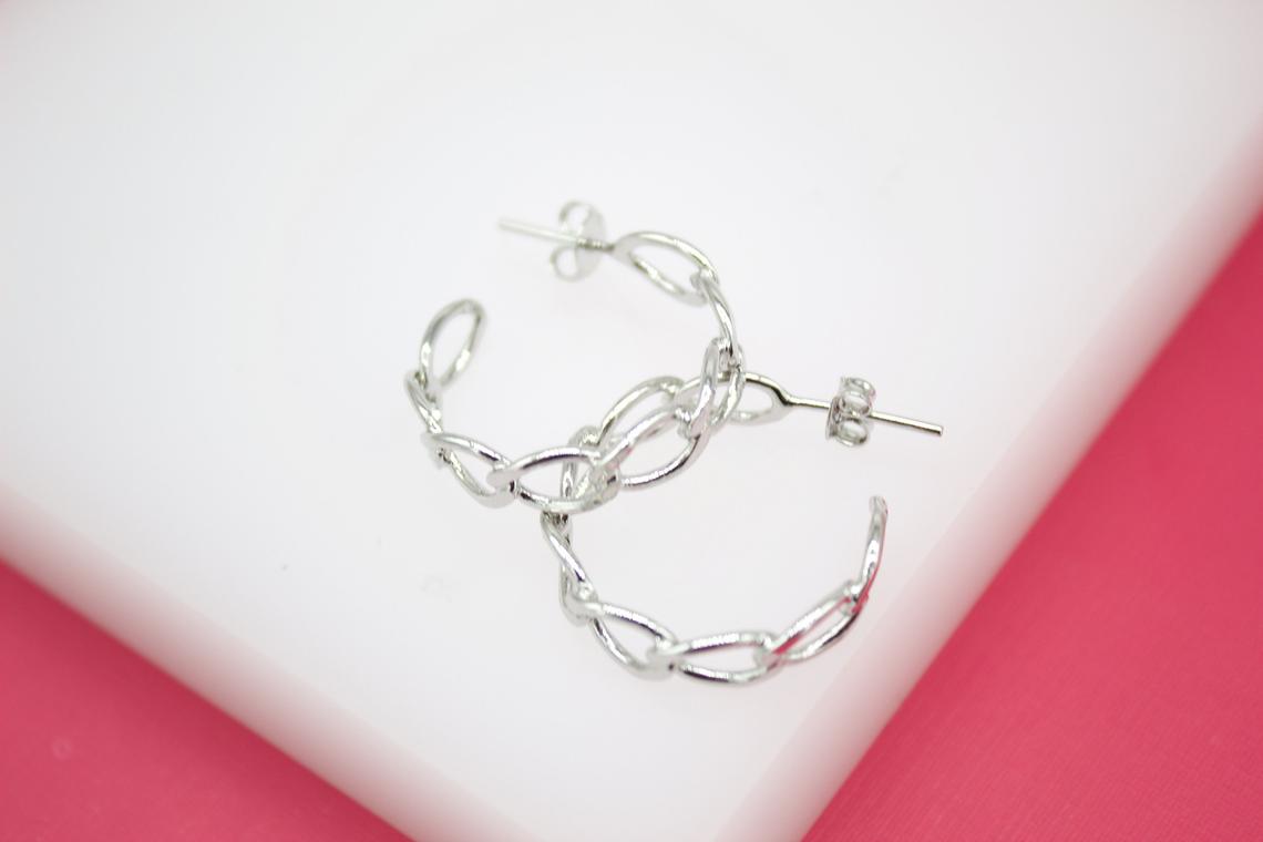 A pair of polished silver chain link hoop earrings rests on a white and pink display surface.