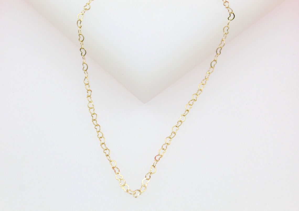 A delicate gold heart chain necklace rests against a neutral white background.