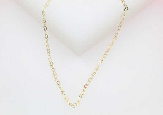 A delicate gold heart chain necklace rests against a neutral white background.