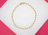 A polished gold ball chain necklace rests in a circle on a white and pink surface.