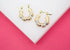 A pair of textured tricolor gold bamboo hoop earrings rests on a white display surface against a vibrant pink background.