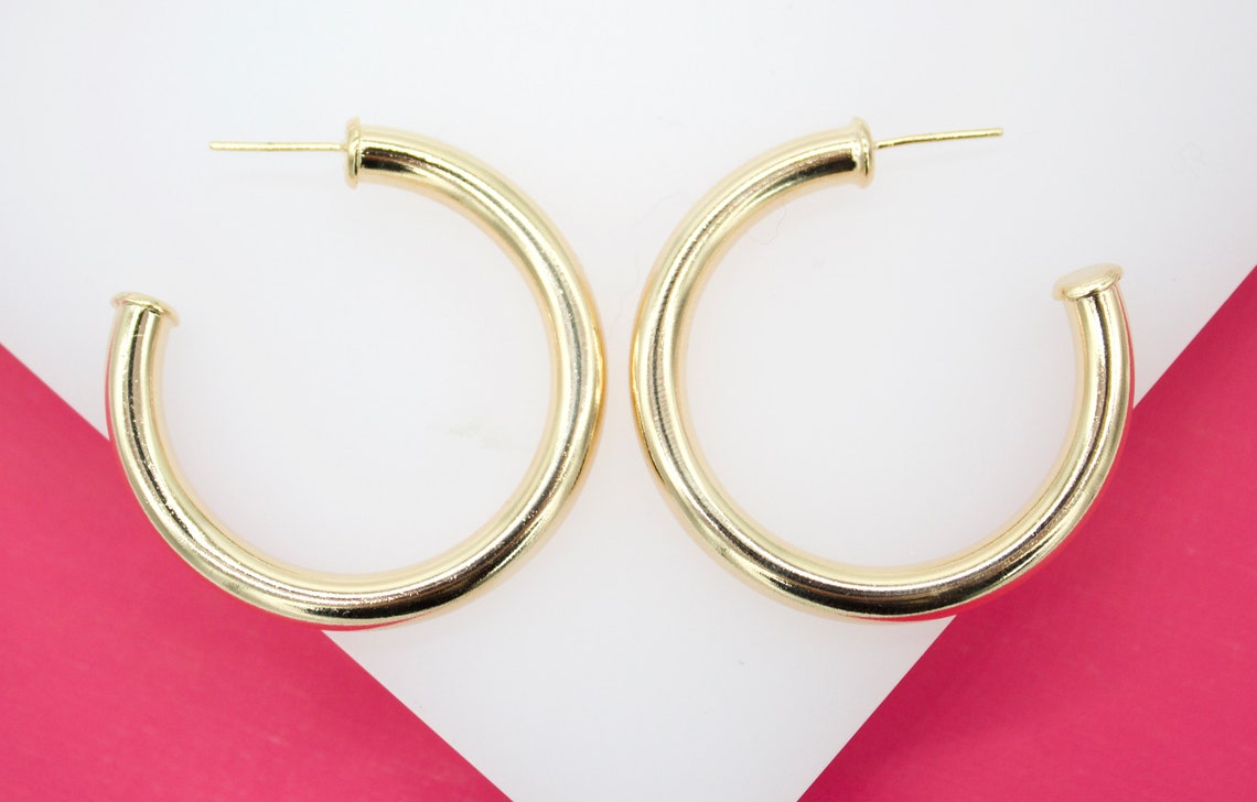 A pair of thick gold hoop earrings rests against a white and pink background.