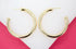 A pair of thick gold hoop earrings rests against a white and pink background.