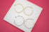 Two pairs of twisted metal hoop earrings in gold and silver rest neatly on a white display block against a vibrant pink background.
