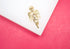 A shiny gold cherub pendant rests on a white display surface against a vibrant pink background.