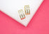 A pair of gold huggie hoop earrings featuring sparkling baguette crystals rests on a white and pink display surface.