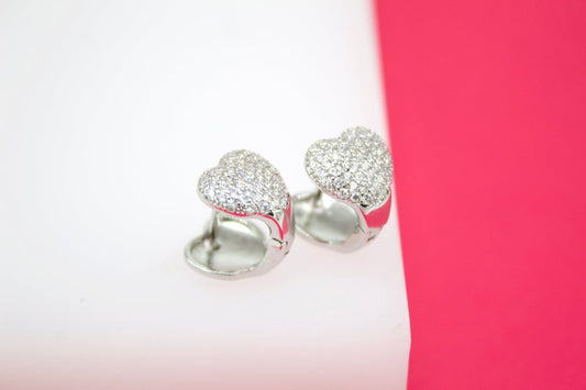 A pair of glittering pave-set heart earrings rests on a white and pink display stand.