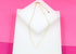 A delicate gold heart-link necklace rests on a white display block against a vibrant pink background.