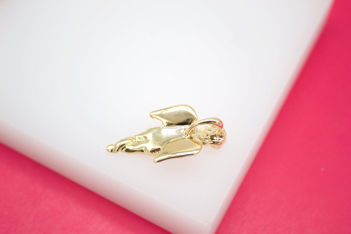 A polished gold angel pendant rests gracefully on a clean white display surface against a vibrant pink background.
