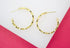 A pair of textured gold hoop earrings rests on a white and pink surface.
