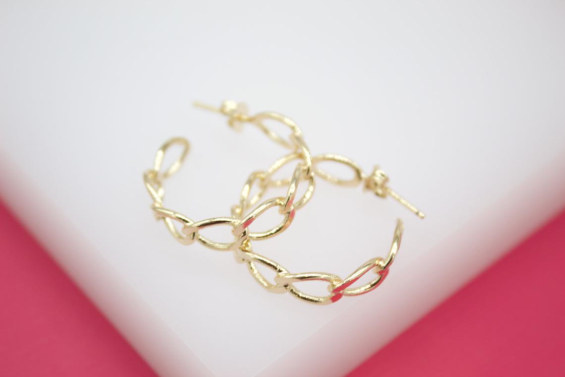 A pair of gold chain link hoop earrings rest on a white surface against a bright pink background.