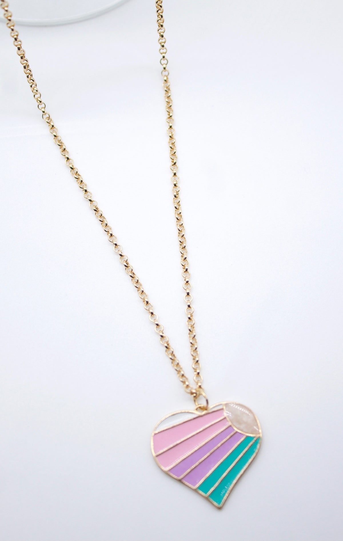 A gold link chain holds a heart-shaped pendant featuring pastel pink, purple, and teal enamel stripes beneath a rising sun motif against a plain white background.