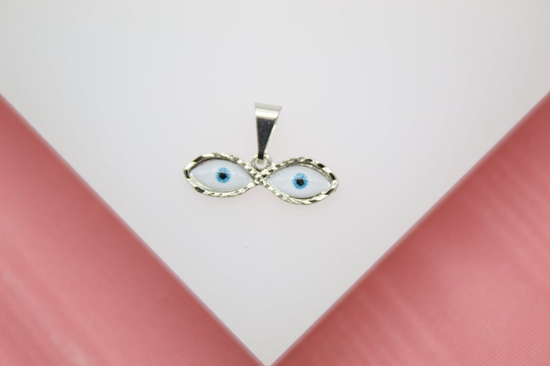 A silver evil eye pendant rests against a white and pink background.