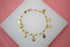 A gold-plated Catholic rosary bracelet featuring small bead accents and hanging Miraculous Medal charms rests on a white display surface.