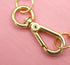 A gold-tone lobster clasp hangs against a pink background, securing jewelry jump rings.