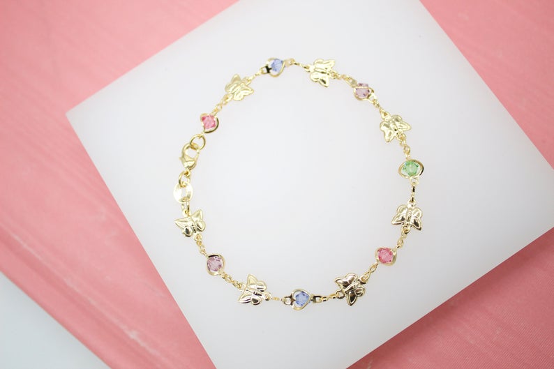 A delicate gold butterfly bracelet features colorful crystal stones arranged in a circular display on a white surface.