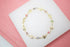 A delicate gold butterfly bracelet features colorful crystal stones arranged in a circular display on a white surface.