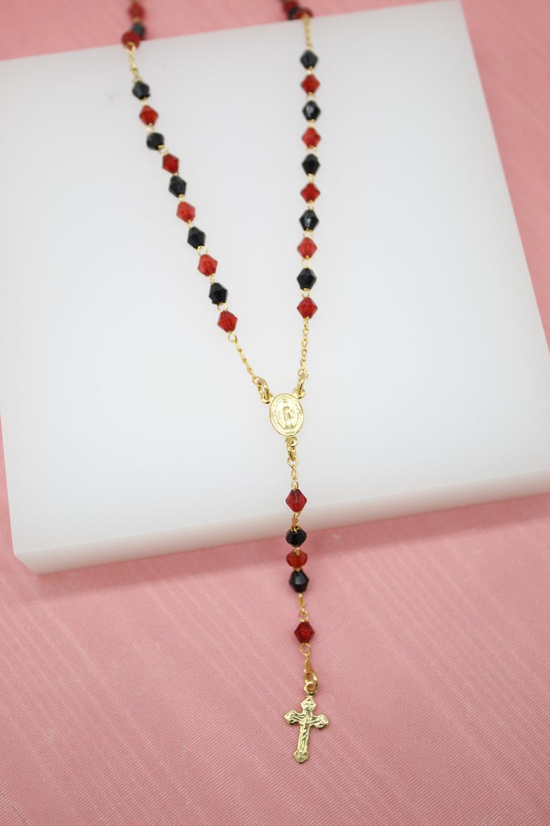A gold Catholic rosary featuring alternating red and black crystal beads rests on a white display block.