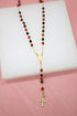 A gold Catholic rosary featuring alternating red and black crystal beads rests on a white display block.