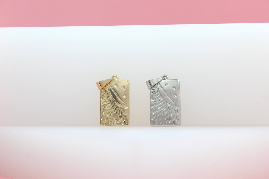 A gold sun and moon rectangle pendant rests beside a silver celestial charm on a white and pink display surface.