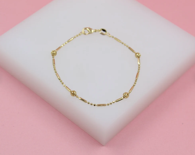 A delicate gold link bracelet rests on a white display stand against a soft pink background.