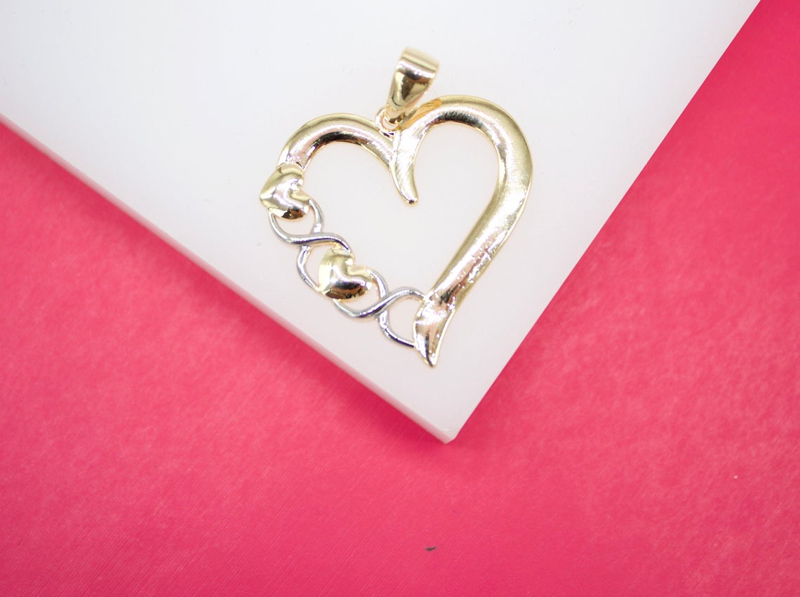 A two-tone gold heart pendant rests on a white display surface against a vibrant pink background.