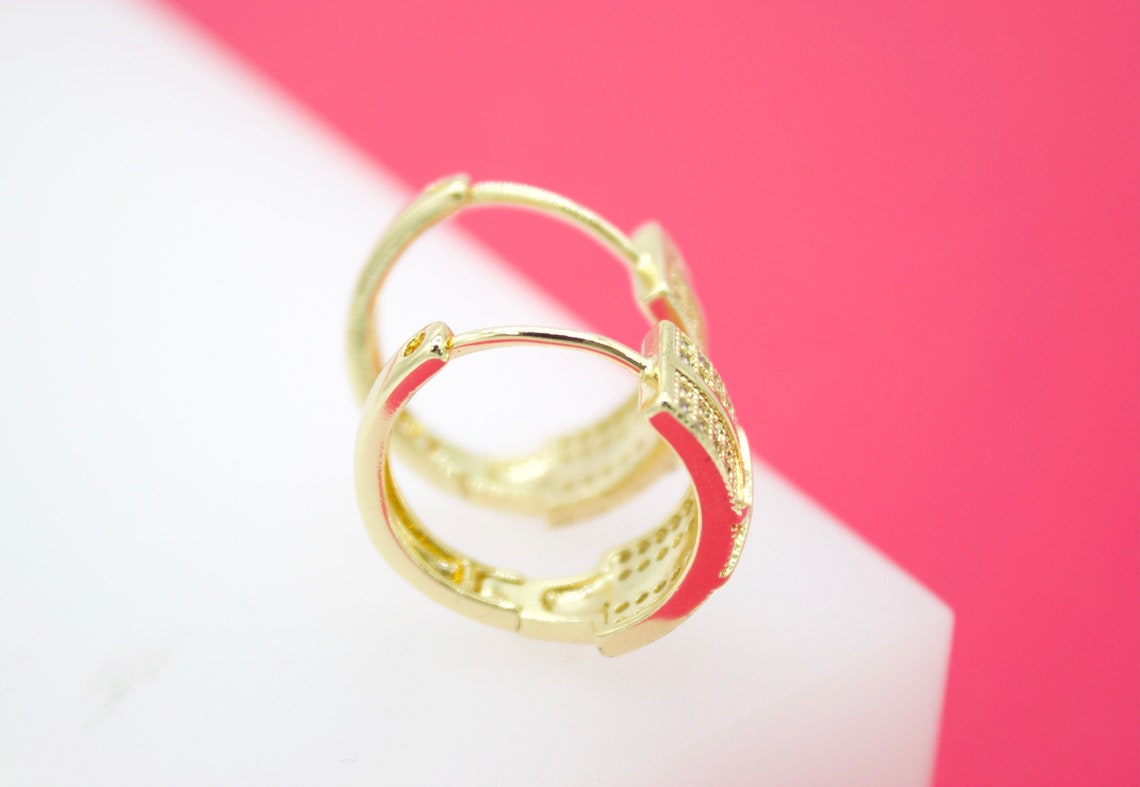 A pair of sparkling gold hoop earrings rests delicately on a white and pink surface.