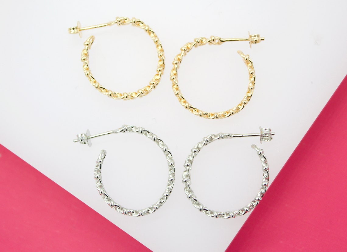 A pair of gold and silver textured hoop earrings rest on a white surface with pink accents.