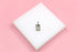 A silver rectangular pendant featuring a sun and stars motif rests on a white display block against a pink background.
