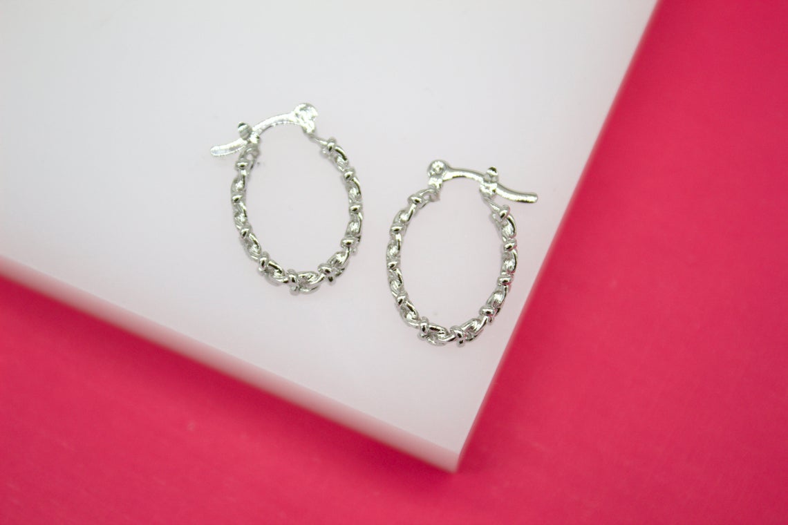 A pair of silver chain-link huggie hoop earrings rests against a pink and white background.