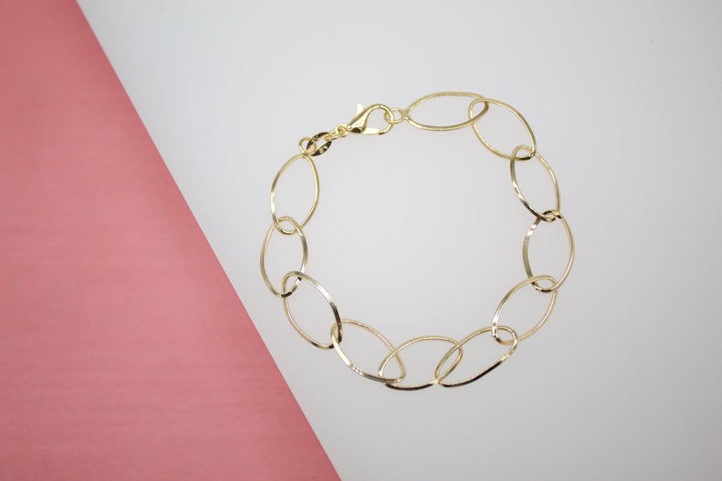 A delicate gold oval link bracelet rests on a white and pink background.
