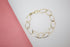 A delicate gold oval link bracelet rests on a white and pink background.