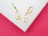A pair of gold padlock drop earrings featuring a heart cutout and sparkling cubic zirconia stones rests on a white and pink display.