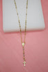 A delicate gold rosary necklace with alternating gold and silver-toned beads rests on a white block against a pink background.