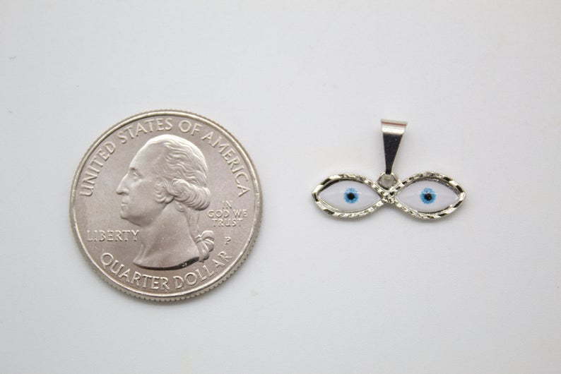 A silver evil eye pendant rests beside a US quarter coin to show its small size.