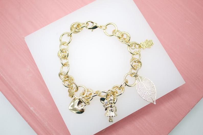 A gold charm bracelet featuring various whimsical pendants rests neatly on a white display surface against a pink background.