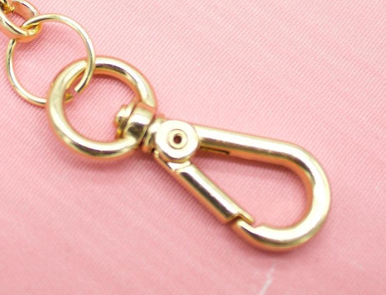 A shiny gold lobster clasp hangs against a soft pink fabric background.