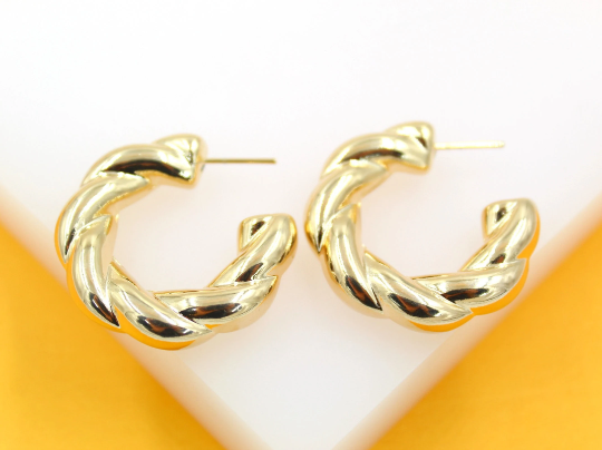 A pair of shiny gold twisted hoop earrings rests on a white and yellow surface.