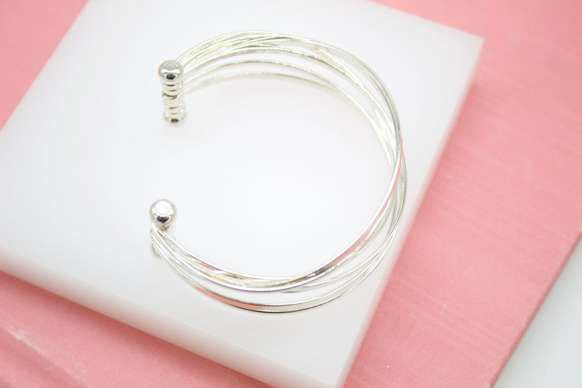 A multi-strand silver cuff bracelet rests on a white display block against a soft pink background.