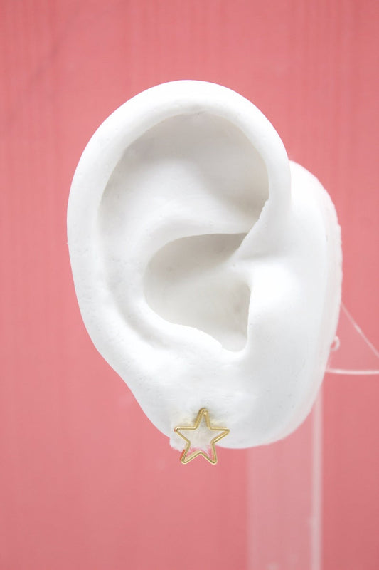 A white mannequin ear displays a delicate gold star stud earring against a pink background.