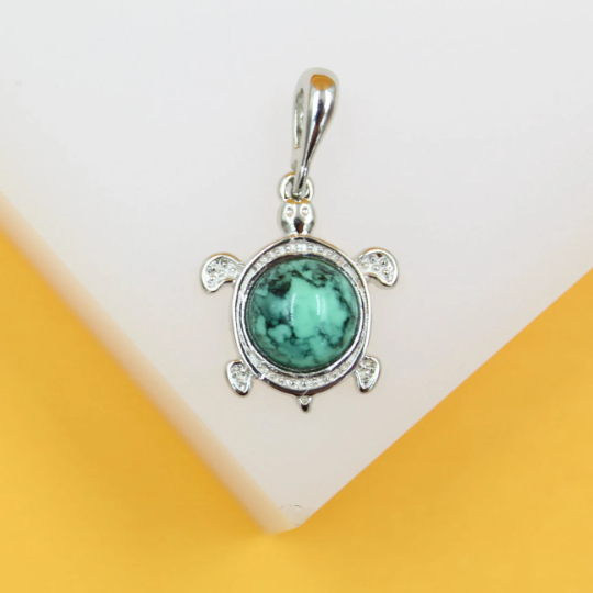 A silver turtle pendant features a round turquoise gemstone shell against a white and yellow background.