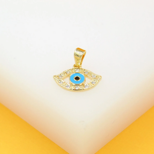 A gold evil eye pendant rests on a white display stand, featuring sparkling cubic zirconia stones and a bright blue enamel center.