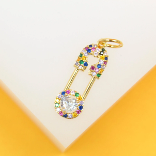 A gold safety pin pendant glitters with multicolored cubic zirconia stones and a central heart-shaped gemstone.