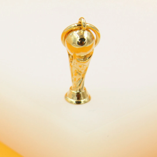A shiny gold World Cup trophy charm stands upright on a light surface.