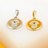 Two round Hamsa hand pendants with evil eye details rest on a surface, one in silver and the other in gold.