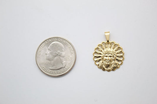 A gold Jesus face pendant rests next to a US quarter coin for size comparison on a light surface.